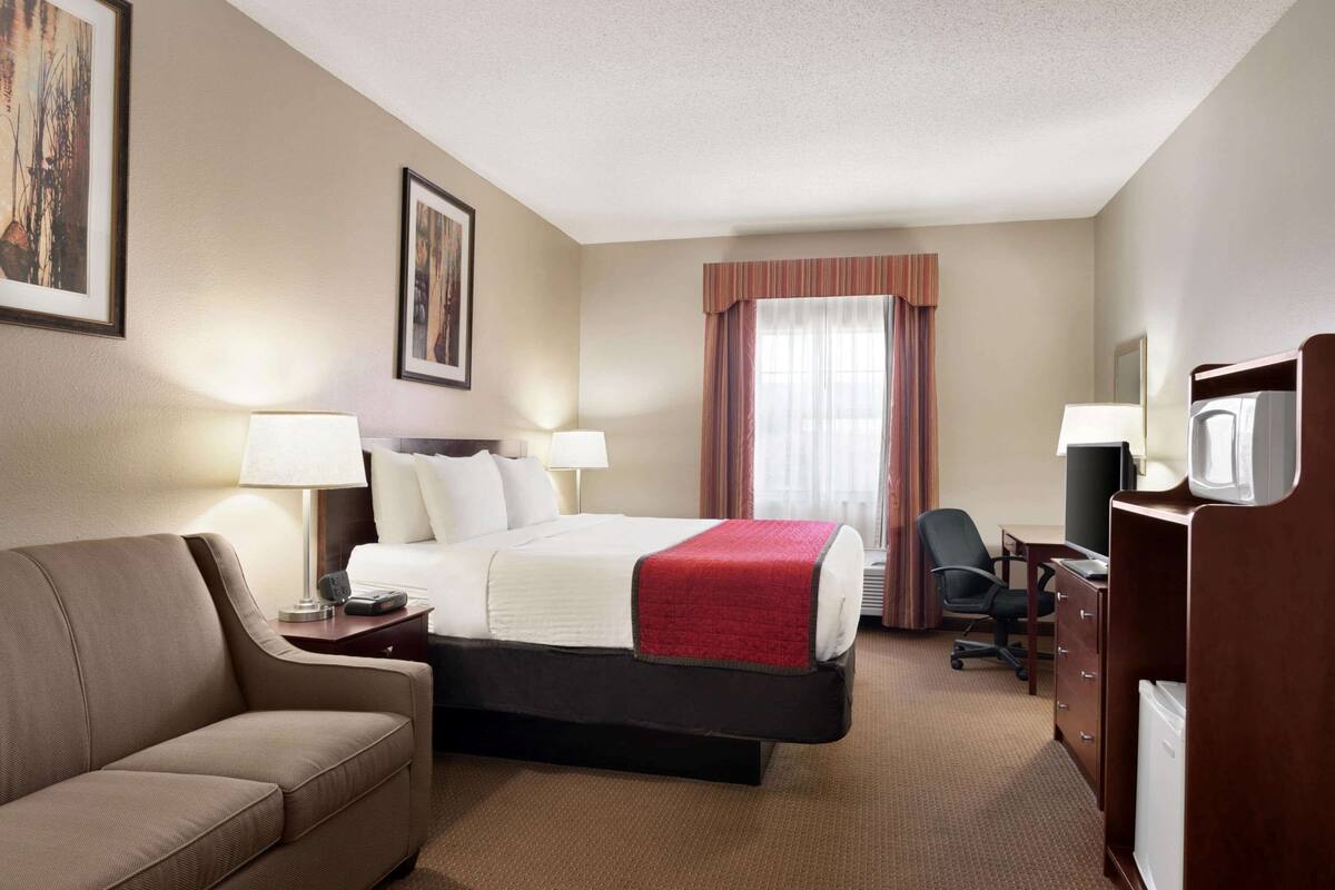 Quarto de hotel com cama, sofá, escrivaninha e televisão.