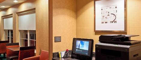 A hotel reception area with a desktop computer, a printer, and a framed architectural photo on the wall.