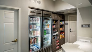 A hotel lobby with a kitchenette area, including two refrigerators stocked with beverages and snacks, a coffee machine, and a sign indicating the manager's duty. - Residence Inn by Marriott Cincinnati Airport Erlanger (Erlanger)