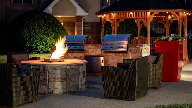 An outdoor patio with stone barbecue grills, wicker furniture, and a gazebo with string lights. - Residence Inn by Marriott Cincinnati Airport Erlanger (Erlanger)