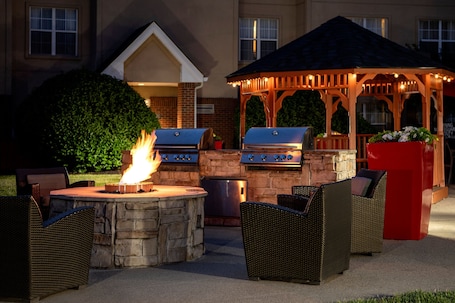 An outdoor patio with stone barbecue grills, wicker furniture, and a gazebo with string lights.