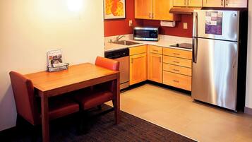 A compact kitchen with wooden cabinets, a stainless steel refrigerator, a microwave, and a dishwasher.