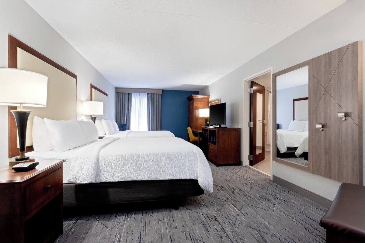 A hotel room with a bed, bedside tables, a desk, a chair, a television, and a mirror.