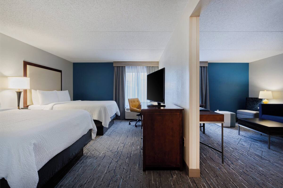 A hotel room with two beds, a desk, a chair, and a television.