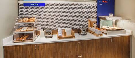 A breakfast station with a bakery display, a sign for breakfast availability, and a sign indicating the method of food preparation.