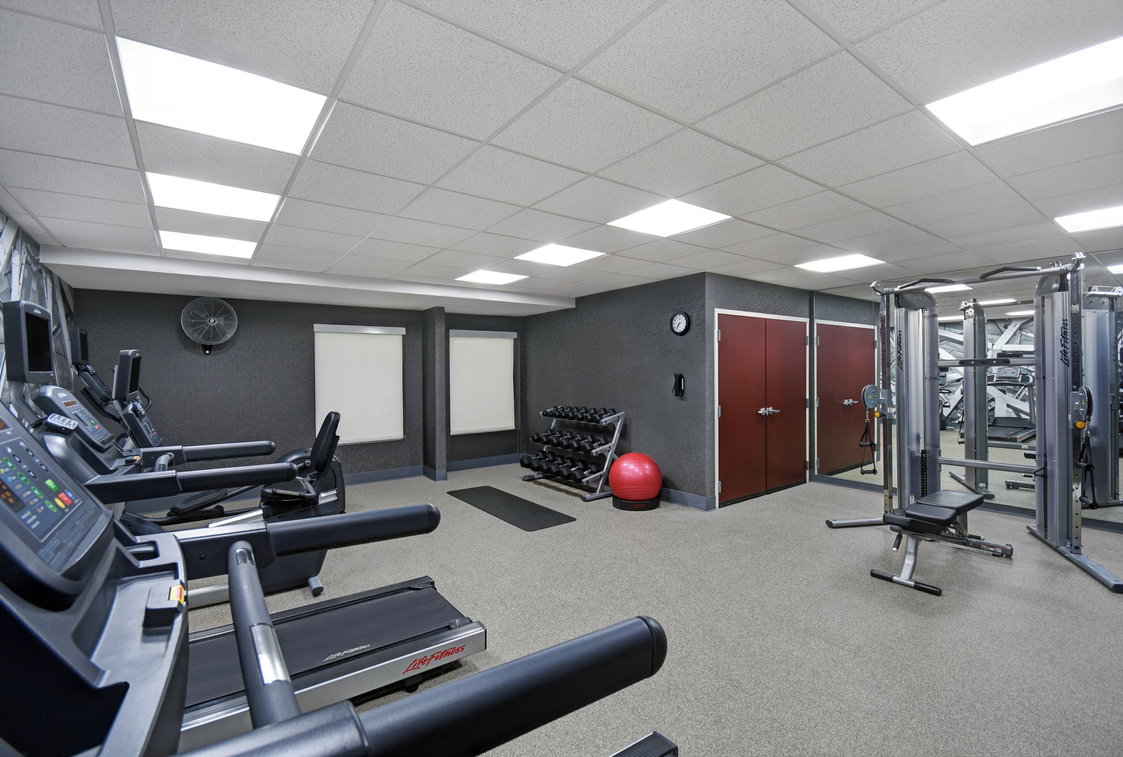 A gym with treadmills, weight machines, and a red exercise ball.