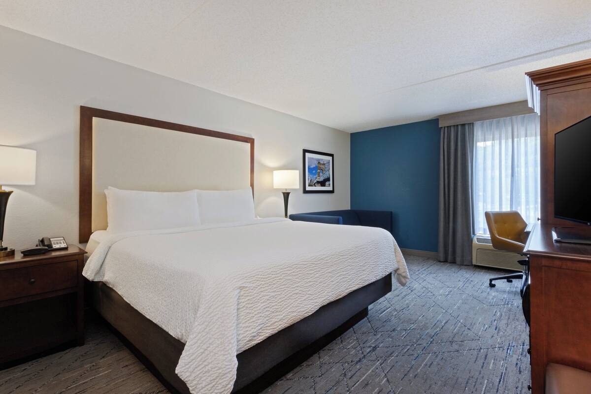 A hotel room with a large bed, a desk with a lamp, a chair, and a television.