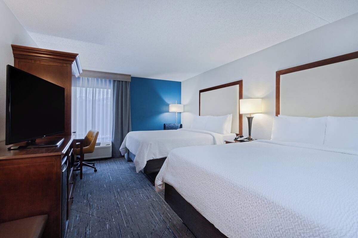 A hotel room with two beds, a TV, a desk, and a chair.