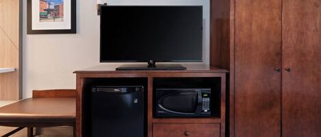 A compact kitchenette with a microwave, a small refrigerator, and a flat-screen TV on a wooden cabinet.