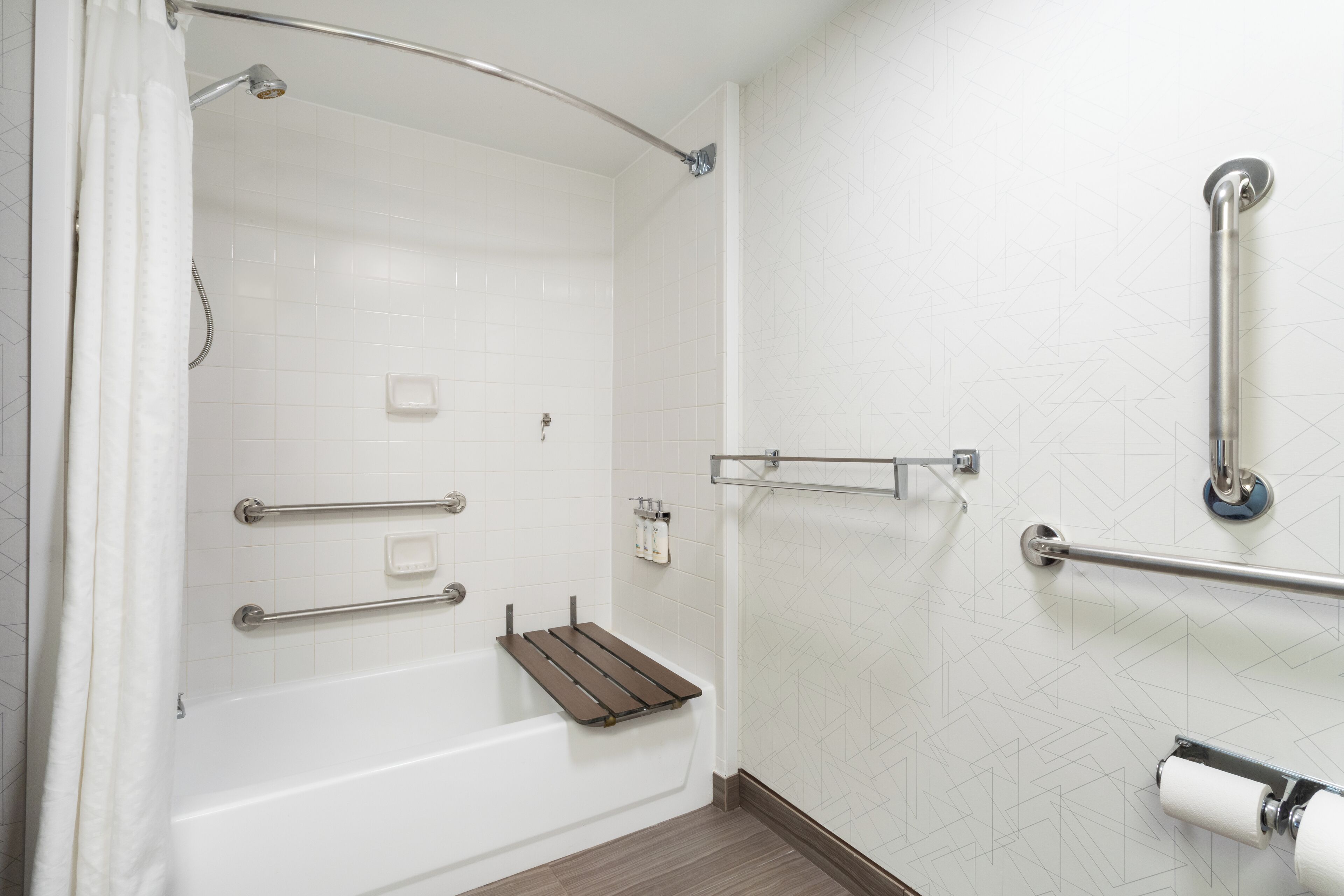 Un baño moderno con cabina de ducha, barras de apoyo y un estante de madera.