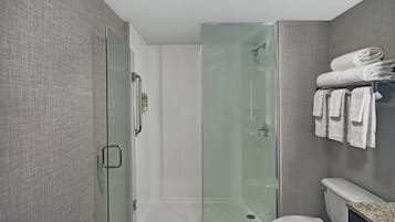 A modern bathroom with a glass-enclosed shower, a toilet, and a towel rack with neatly folded towels.