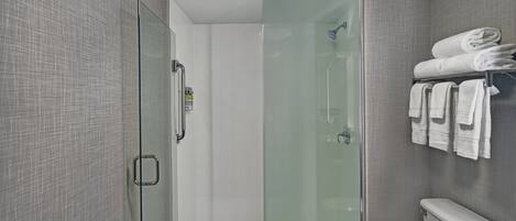 A modern bathroom with a glass-enclosed shower, a toilet, and a towel rack with neatly folded towels.