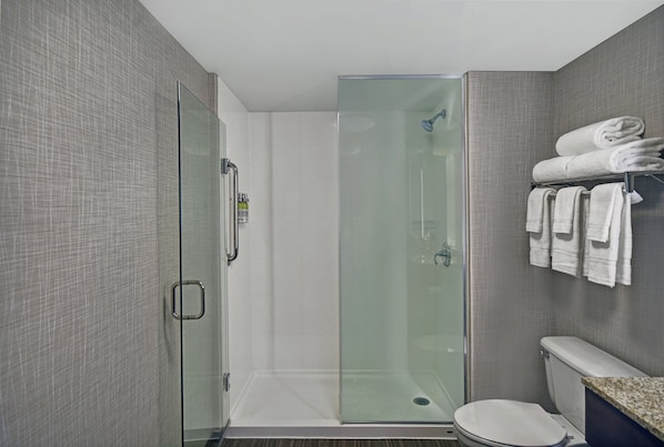 A modern bathroom with a glass-enclosed shower, a toilet, and a towel rack with neatly folded towels. - Holiday Inn Express & Suites Cincinnati Riverfront by IHG (Covington)