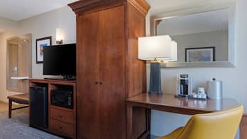 A hotel room with a wooden cabinet, a television, a microwave, a coffee maker, and a yellow chair.