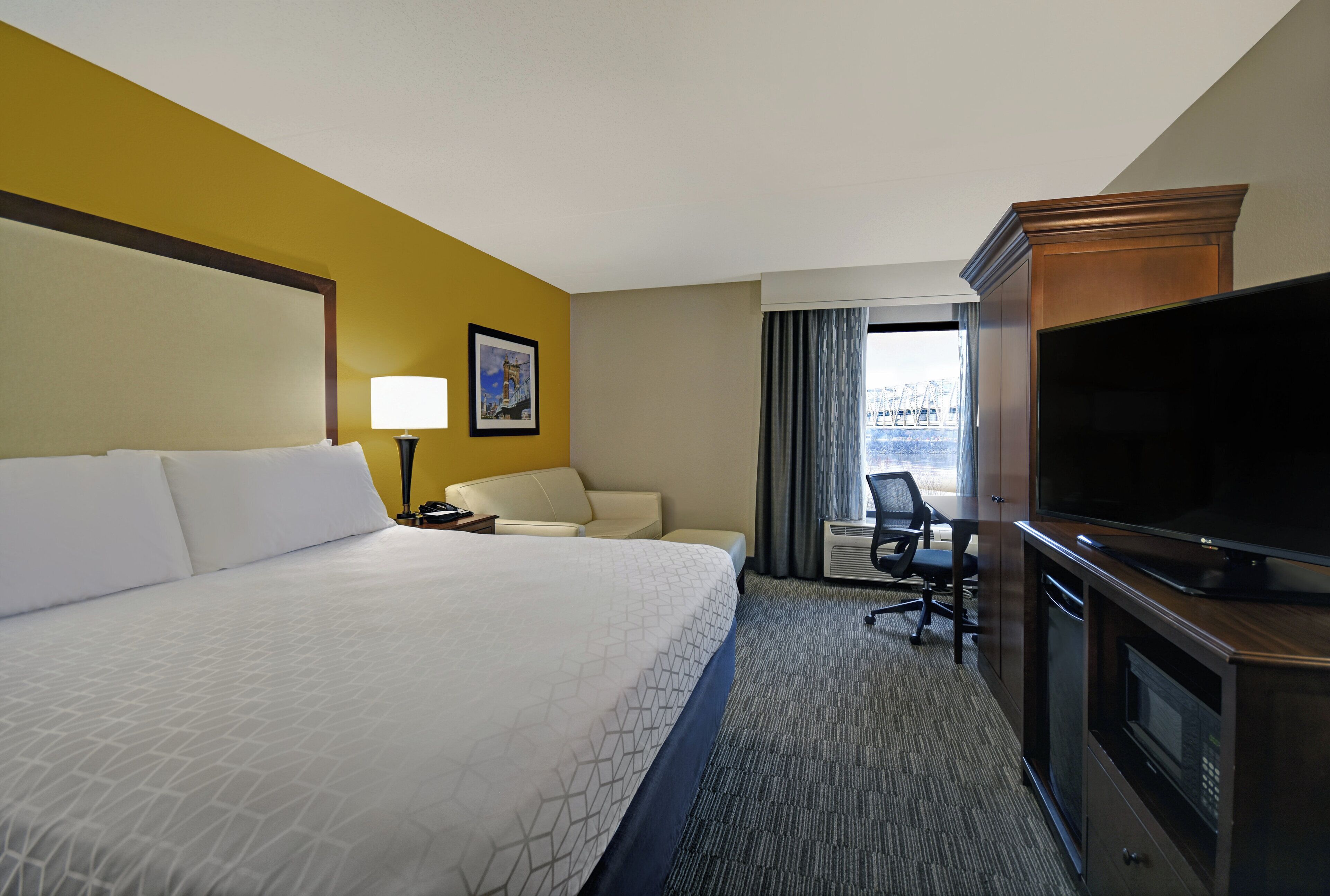A hotel room with a large bed, a desk with a chair, a television, and a window with curtains.