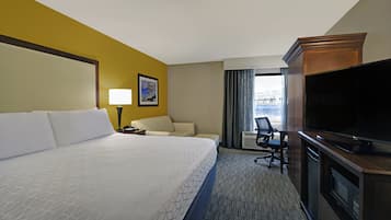 A hotel room with a large bed, a desk with a chair, a television, and a window with curtains.