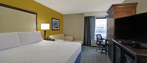 A hotel room with a large bed, a desk with a chair, a television, and a window with curtains.