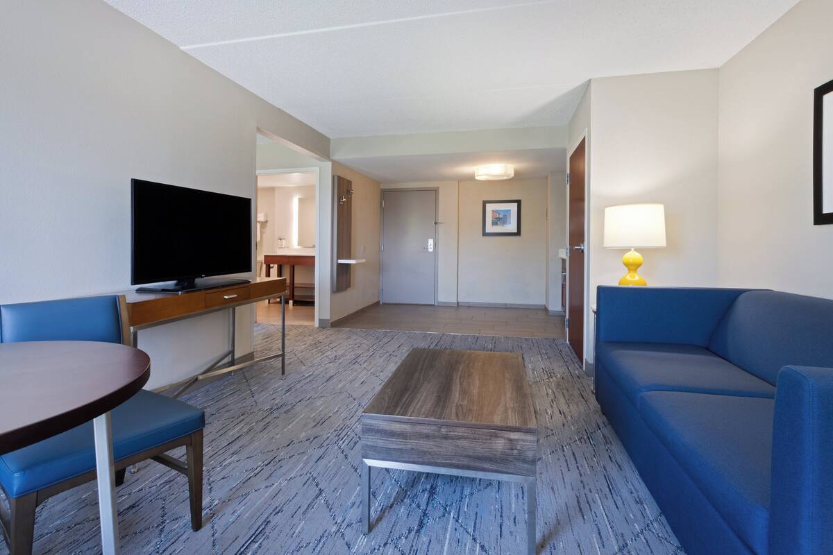 A hotel room with a television, a blue sofa, a small table, and a lamp.