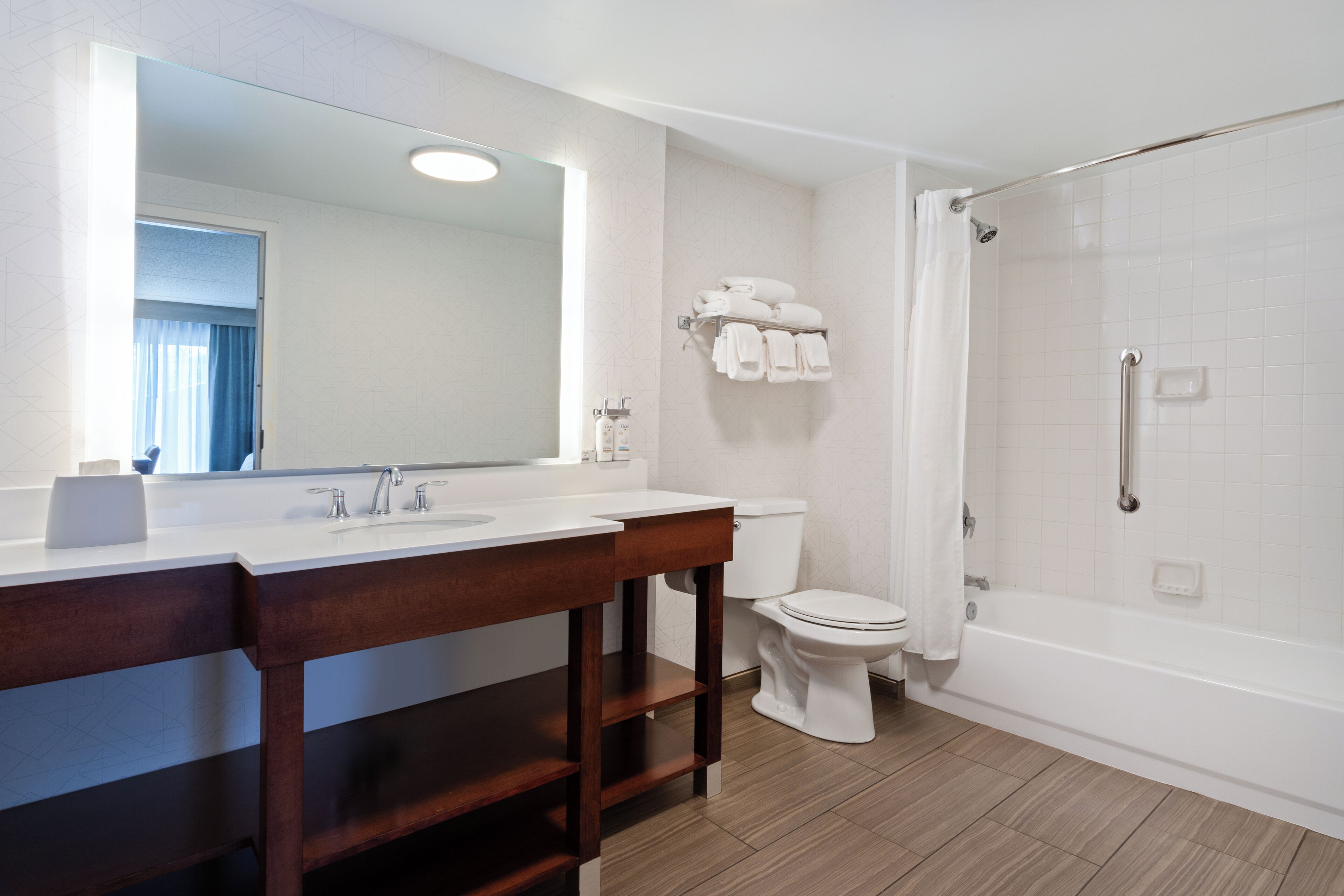 Un baño moderno con tocador de madera, un espejo grande, inodoro y ducha a ras de suelo.