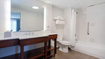 Un baño moderno con tocador de madera, un espejo grande, inodoro y ducha a ras de suelo.