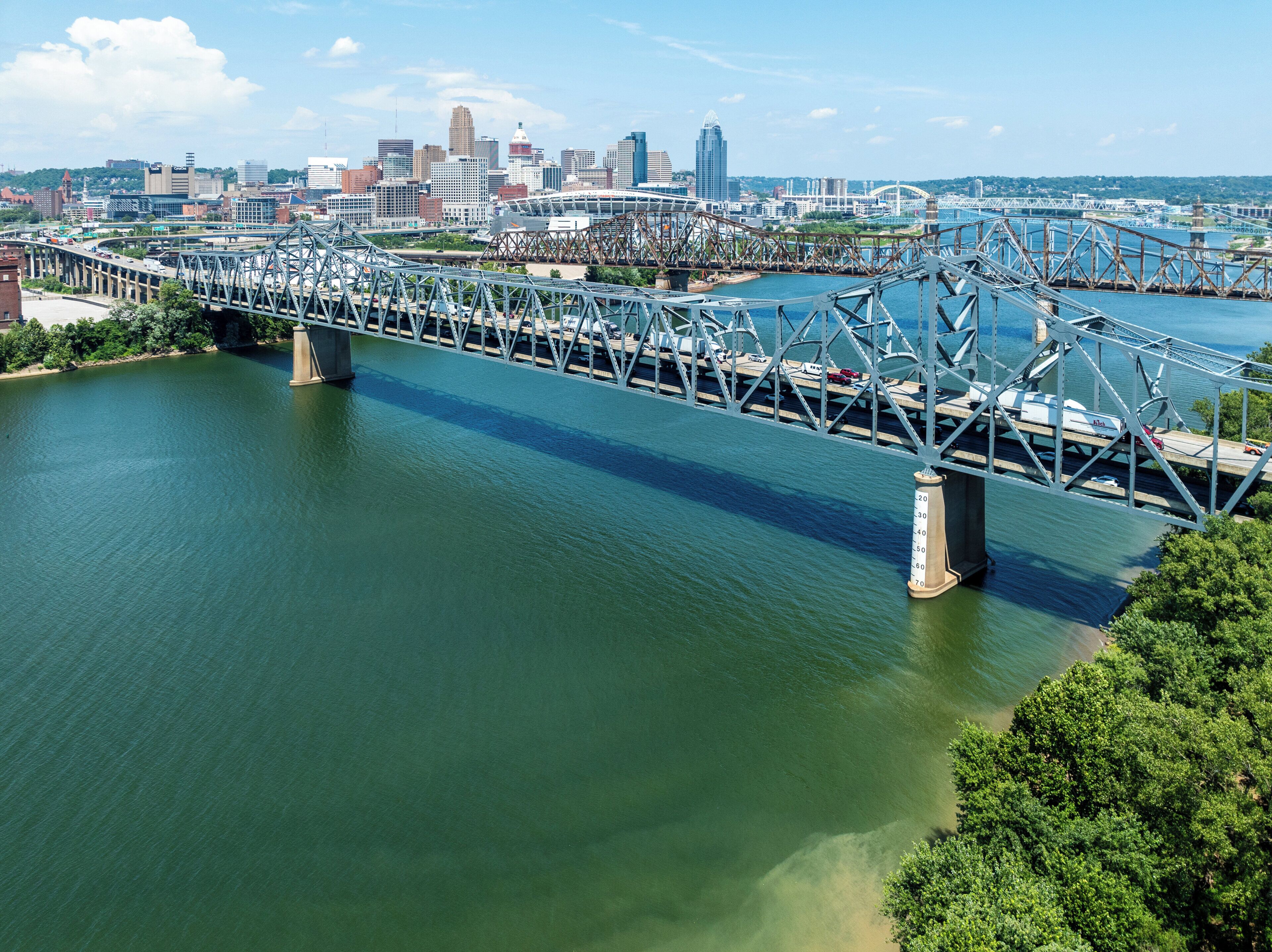 A large steel bridge spanning a river with a city skyline in the background.