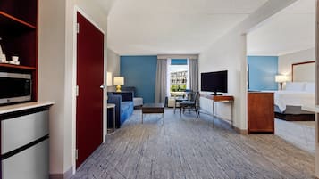 Quarto de hotel com cama, escrivaninha, televisão, sofá, mesa de jantar e vista para o exterior.