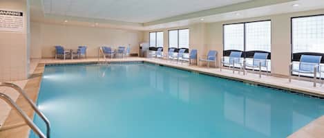 A large indoor swimming pool with clear blue water, surrounded by lounge chairs and a tiled floor.
