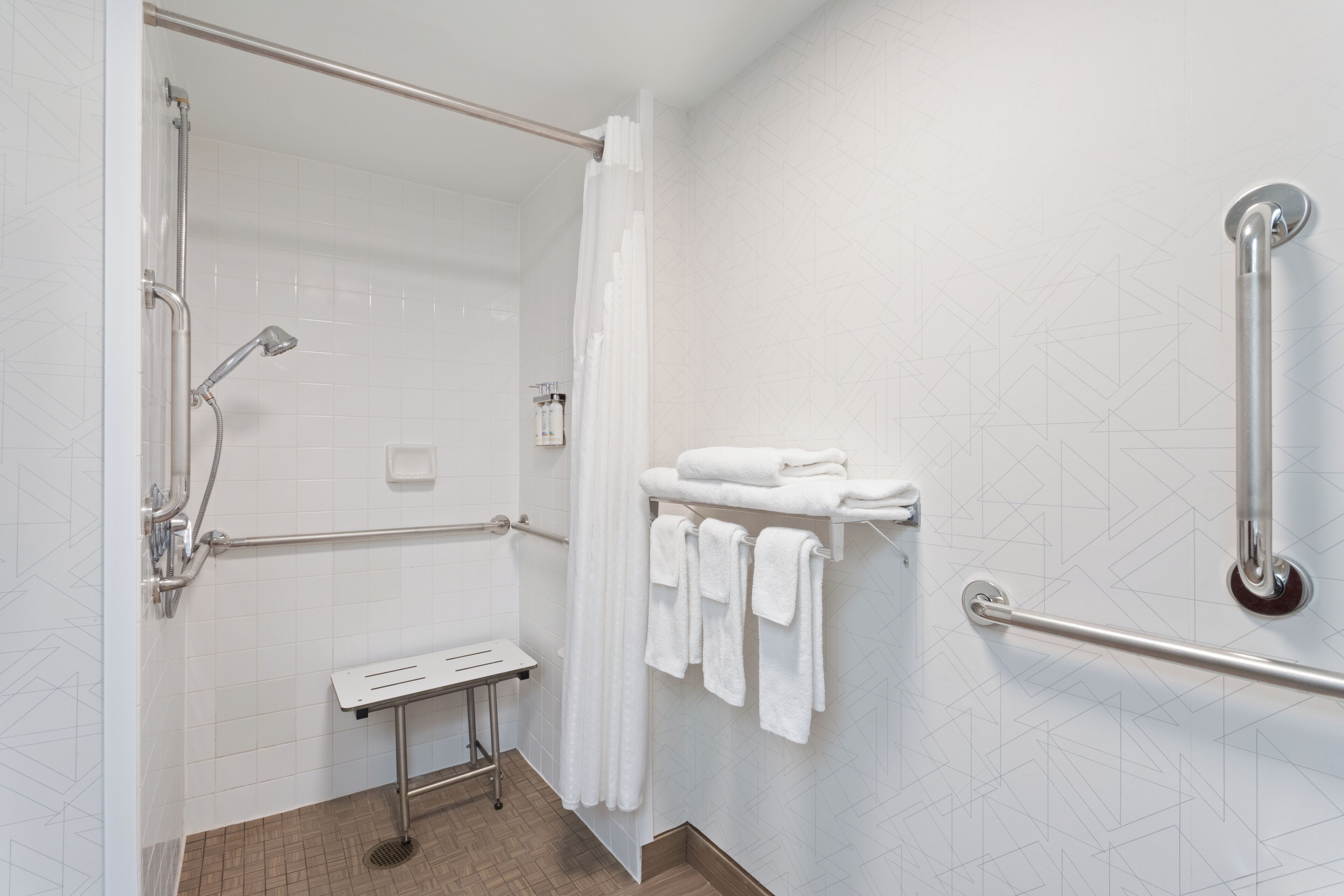 A modern bathroom with a walk-in shower, grab bars, a towel rack, and a small bench.