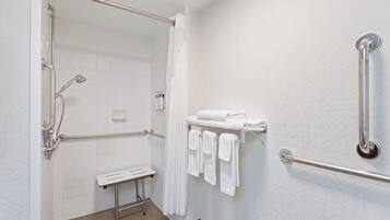 A modern bathroom with a walk-in shower, grab bars, a towel rack, and a small bench.