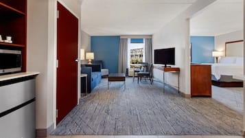 A hotel room with a bed, a desk with a TV, a sofa, a coffee table, and a microwave.