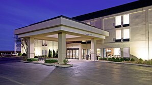 A modern hotel entrance with a covered waiting area, a clear sign indicating the entrance, and a well-lit facade.