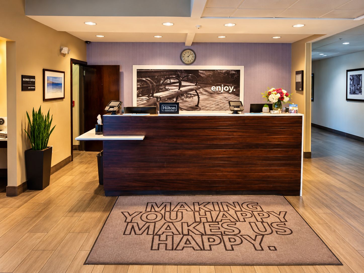 Een hotel receptiebalie met een klok, een ingelijst beeld en een welkomstmat.