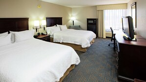 A hotel room with two beds, a desk with a television, a lamp, and a clock on the wall.