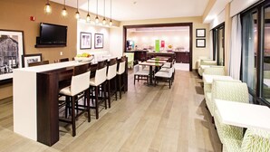 A modern hotel dining area with a long bar, multiple dining tables, and chairs.