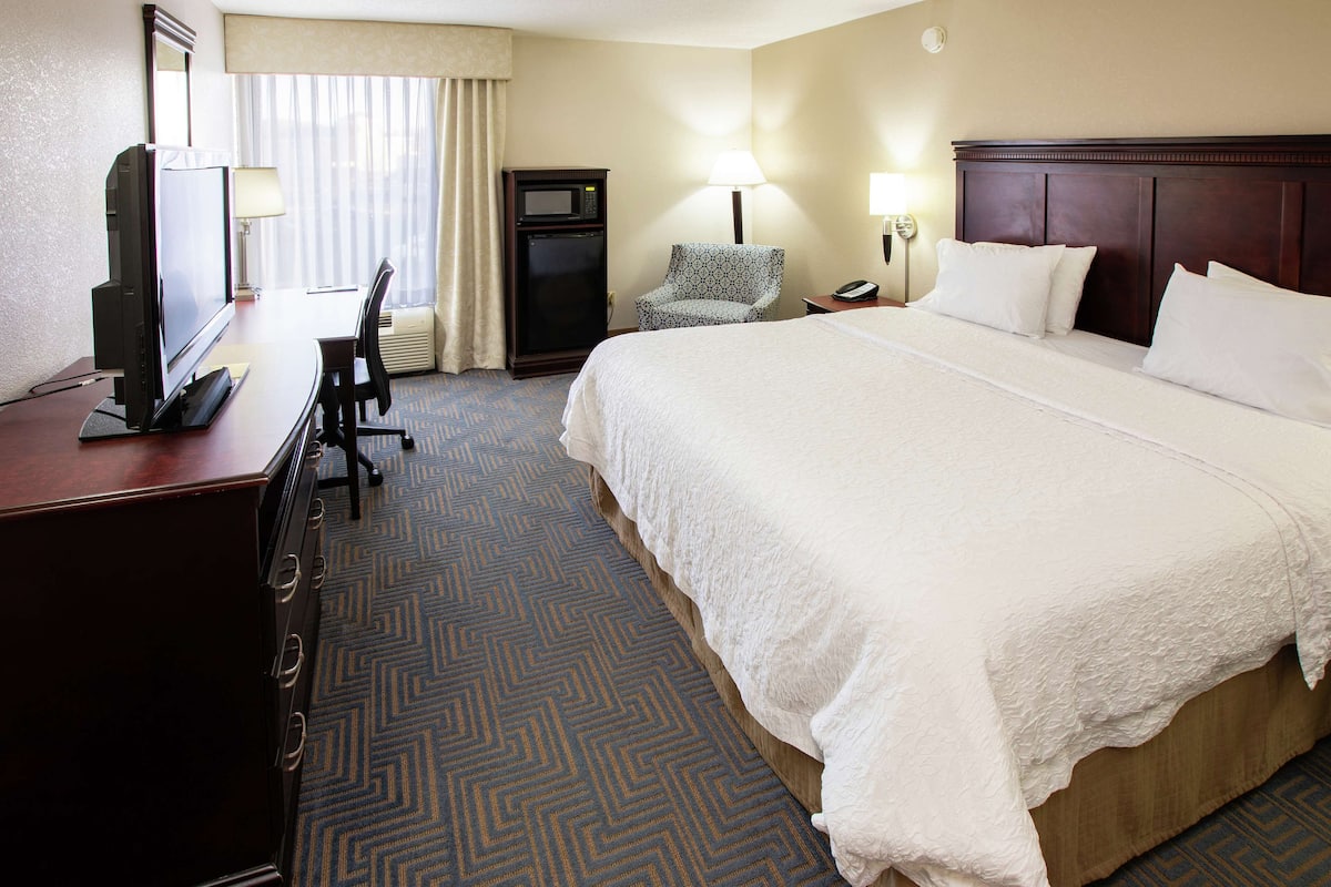 A hotel room with a large bed, a desk with a television, a chair, a microwave, and a lamp.