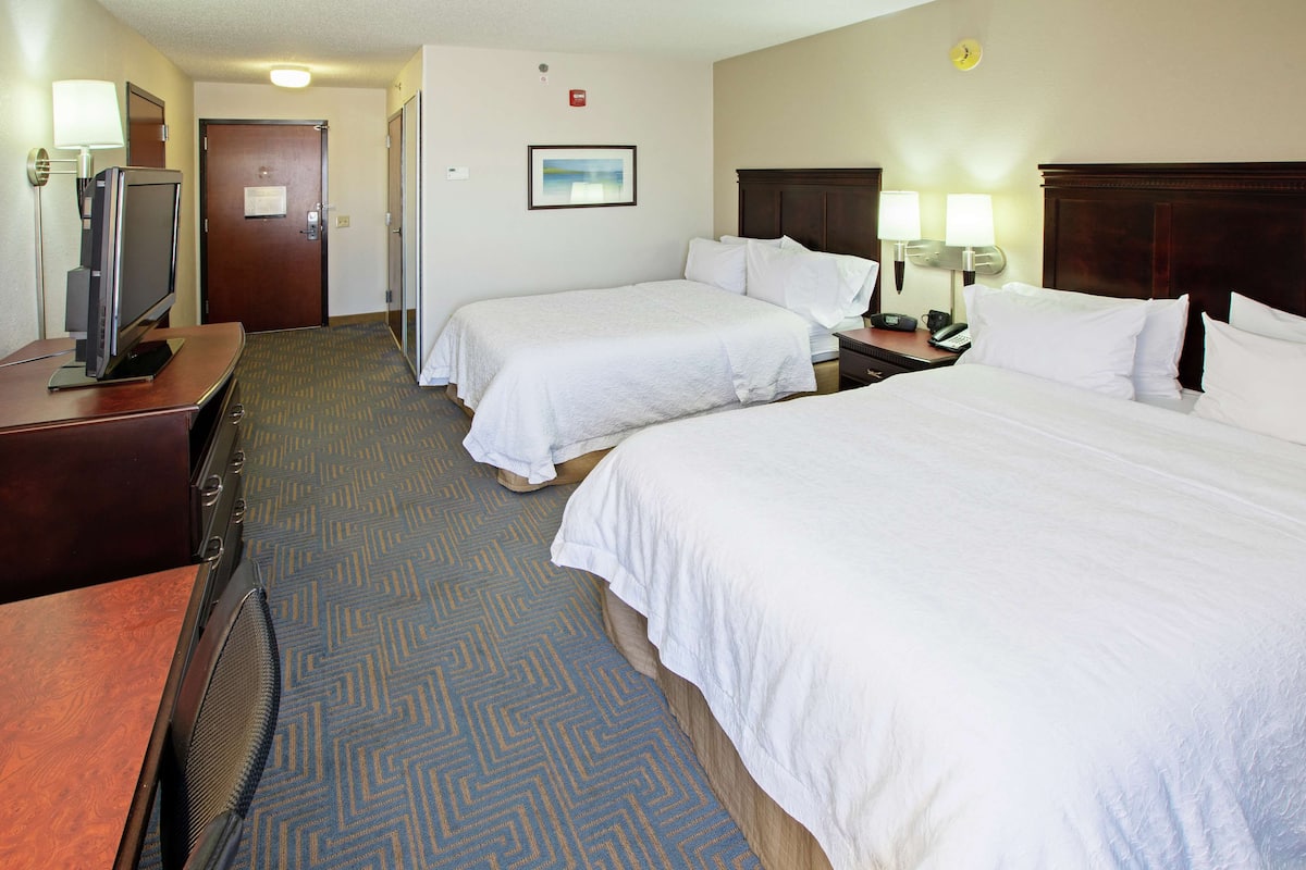 A hotel room with two beds, a desk with a television, and a carpeted floor.