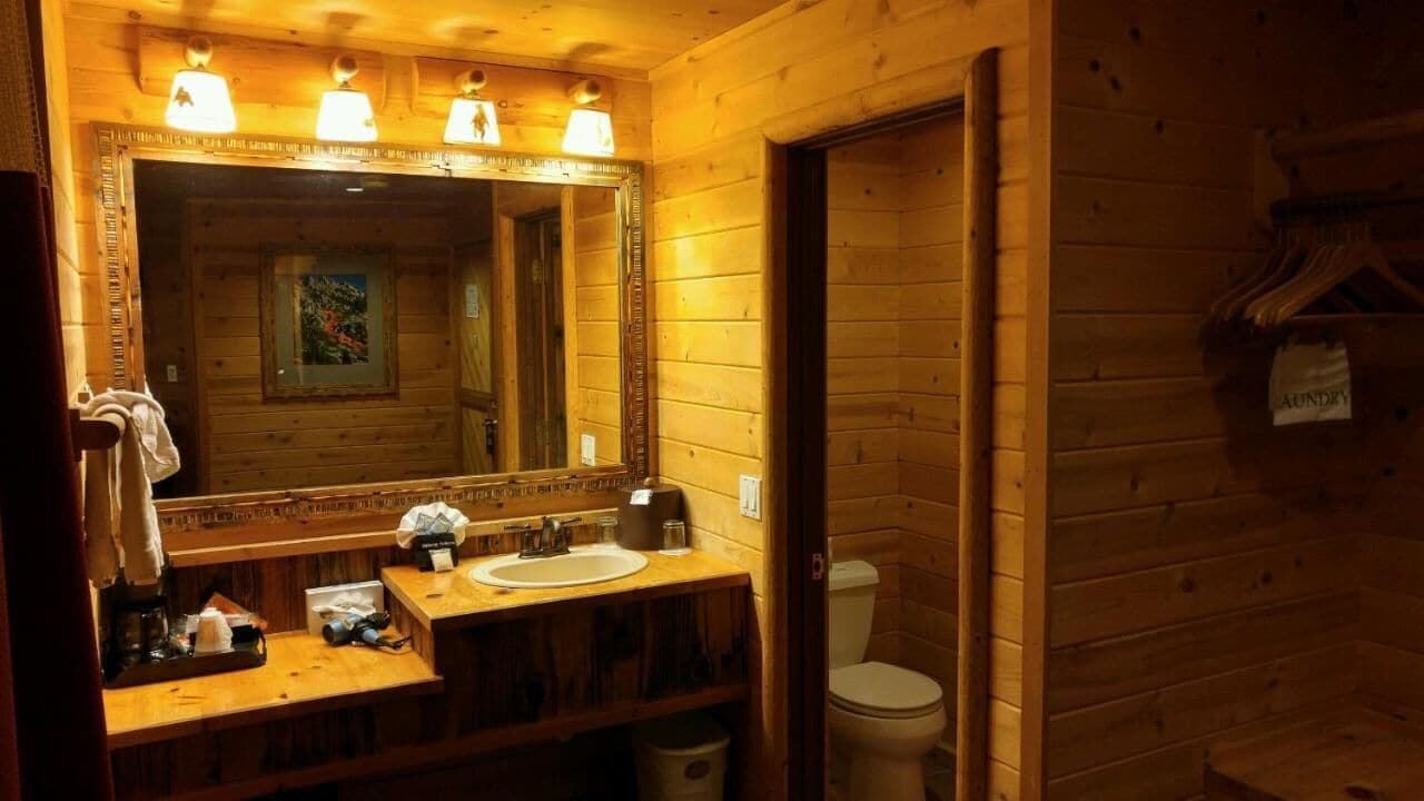Un bany d'estil cabana de fusta amb un mirall gran, un lavabo i un vàter.