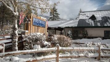 Un letrero de madera anuncia Postmarc hotel & spa suites, rodeado de plantas cubiertas de nieve y una valla de madera.