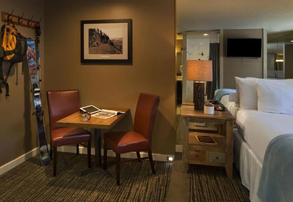 Habitación de hotel con cama, escritorio con silla, lámpara y una tabla de snowboard apoyada en la pared.