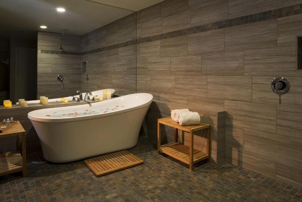 A modern bathroom with a freestanding bathtub, wooden side tables, and a tiled floor.