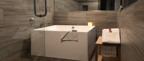 A modern bathroom with a large bathtub, a wooden bench, and a mirror.