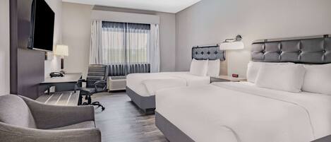 Une chambre d’hôtel avec deux lits, une télévision, un bureau avec une lampe et une chaise.