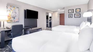 A hotel room with two beds, a desk with a chair, a television, and a painting on the wall.