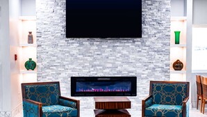 Una sala de estar moderna con chimenea, dos sillones estampados, una mesa de centro y un televisor de pantalla plana montado en una pared de piedra.