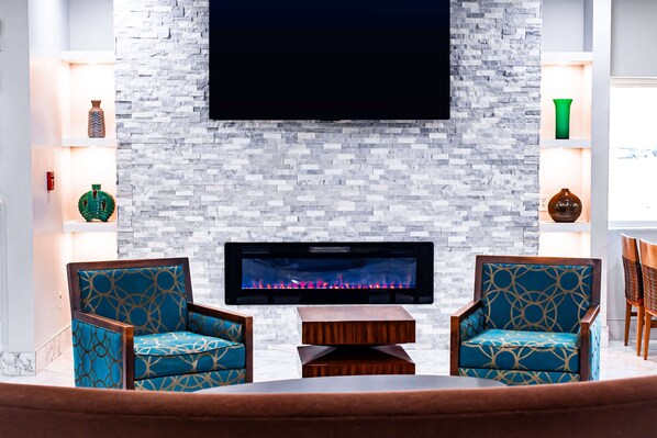 Una sala de estar moderna con chimenea, dos sillones estampados, una mesa de centro y un televisor de pantalla plana montado en una pared de piedra.