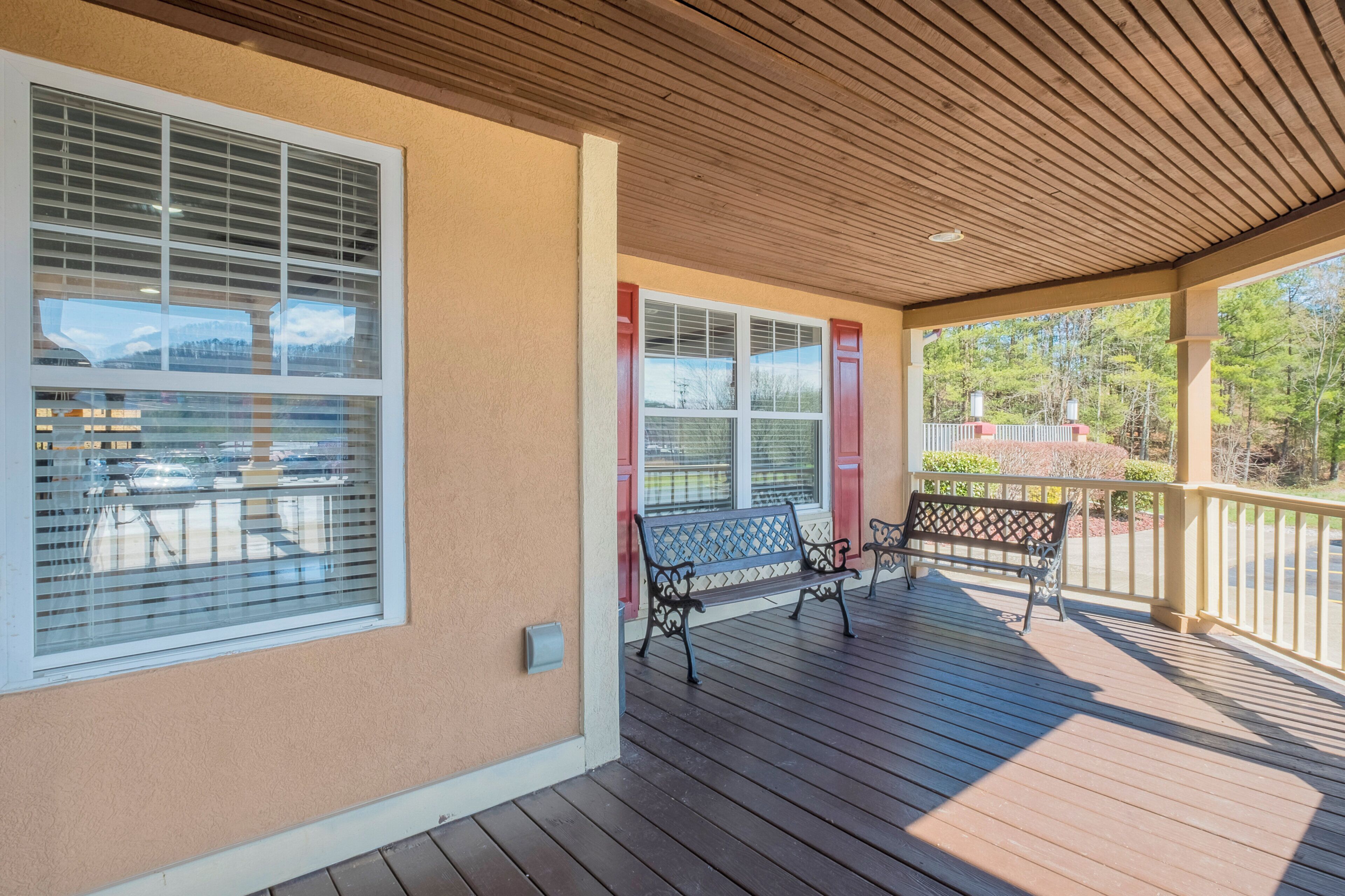 A covered porch with wooden flooring, two benches, and large windows with blinds.