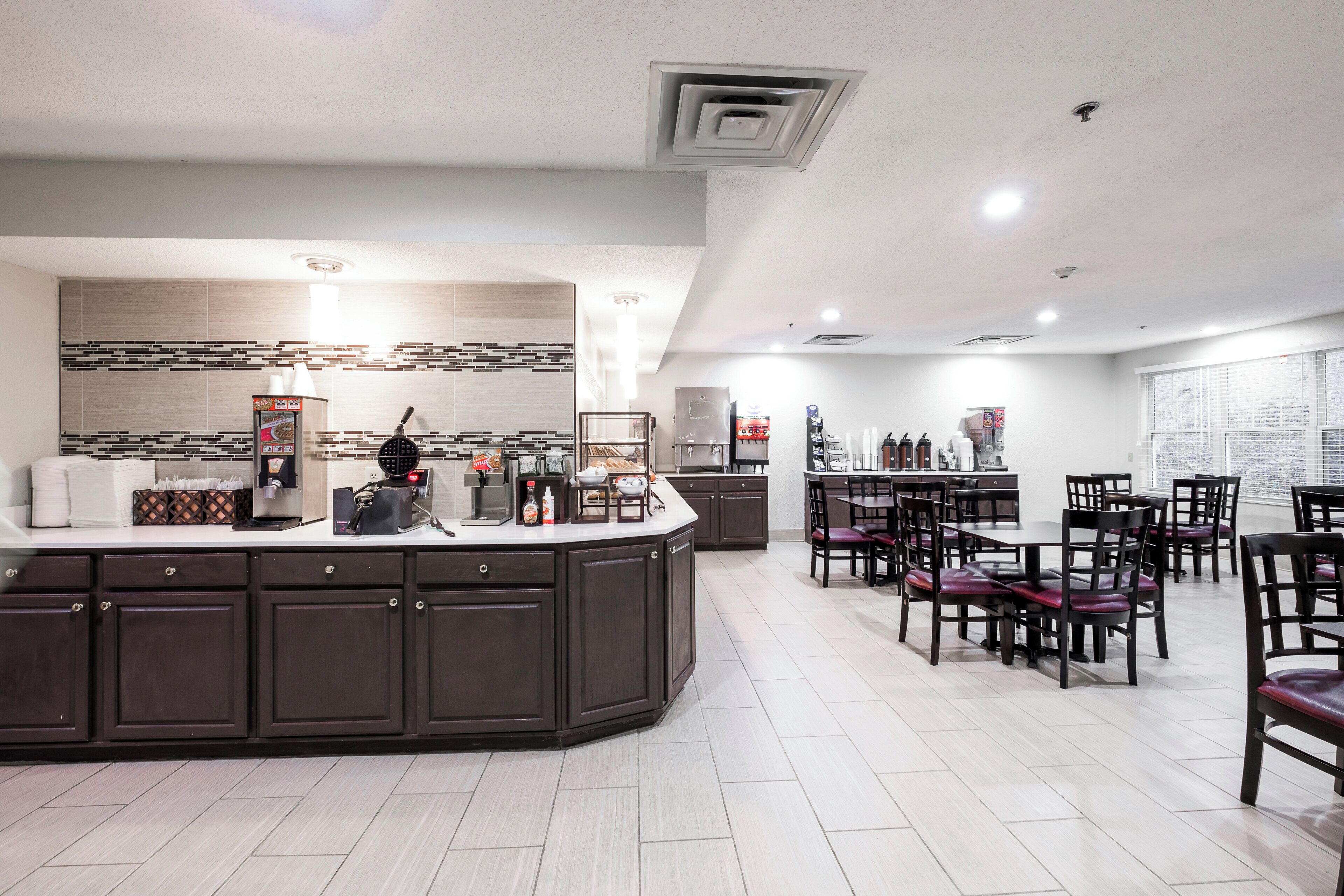 A modern kitchen with a central island, dark cabinetry, and a dining area with multiple chairs and tables.