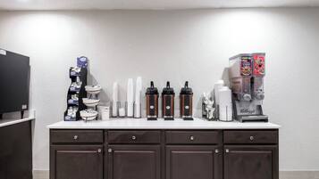 Una kitchenette equipada con cafetera, dispensador de té y refrigerador.