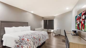 Ett hotellrum med en stor säng, ett skrivbord med en platt-TV, en sittgrupp med en stol och ett fönster med gardiner.