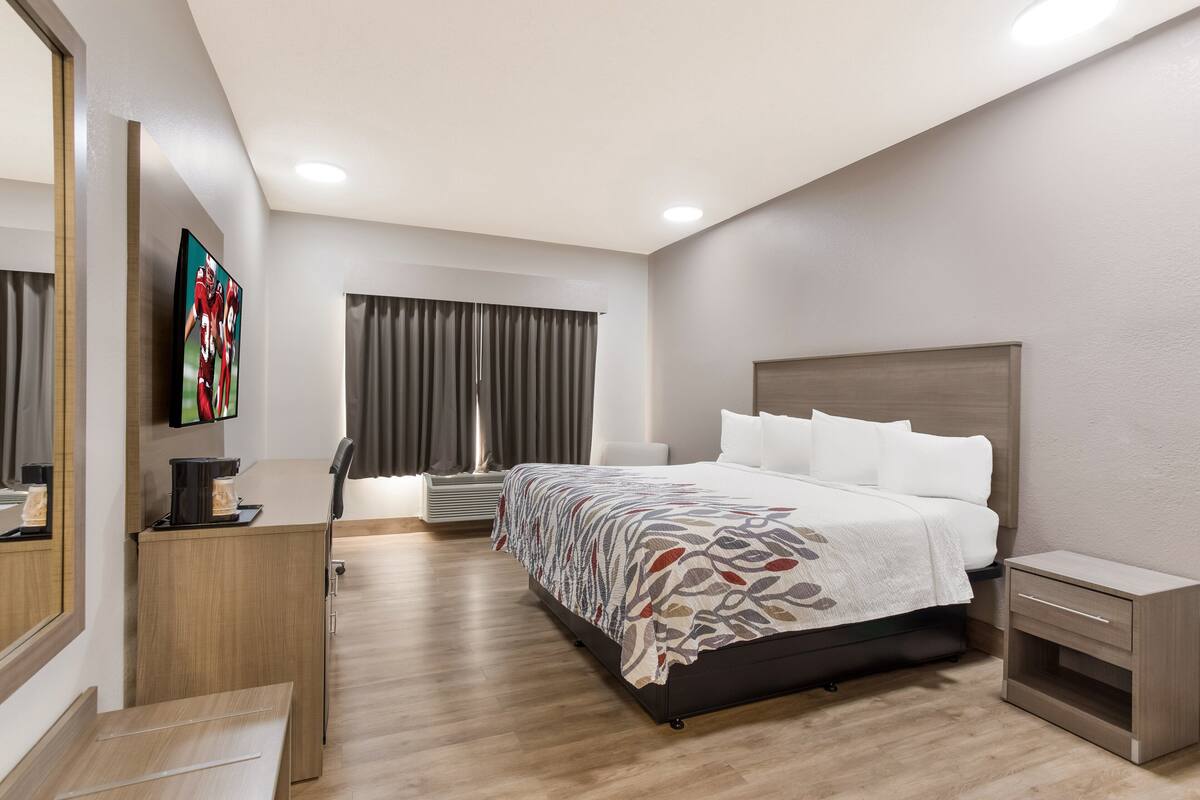 Una habitación de hotel moderna con una cama grande, un escritorio con cafetera, un televisor y una ventana con cortinas.
